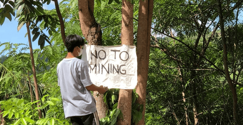 Climate justice defender hanging a sign in a tree that says 'no to mining'